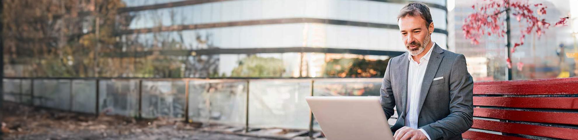 Un homme en costume sur un banc rouge qui consulte son ordinateur