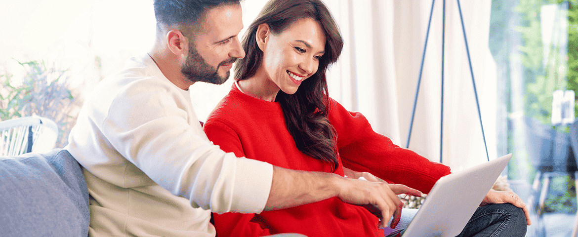un couple assis sur un canapé, concentré sur l’écran d’un ordinateur portable