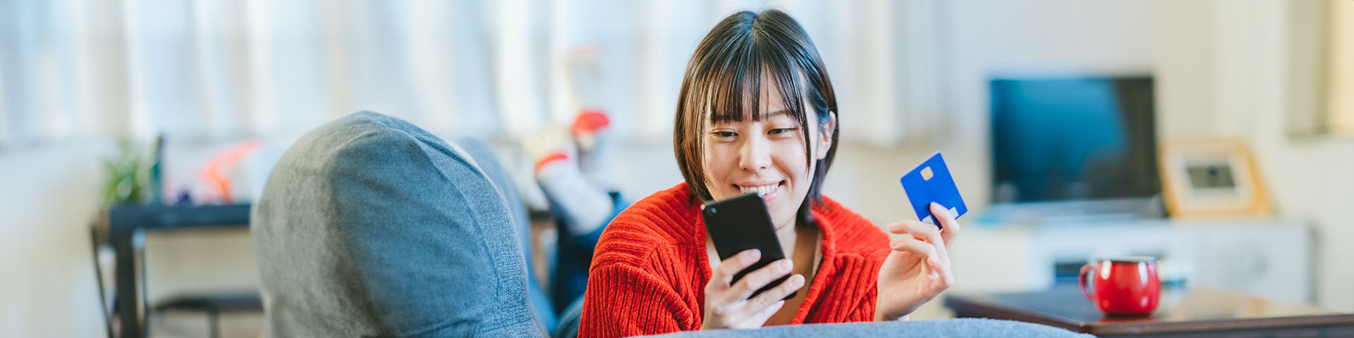 Une femme qui regarde son téléphone et qui a sa carte bleue dans la main gauche