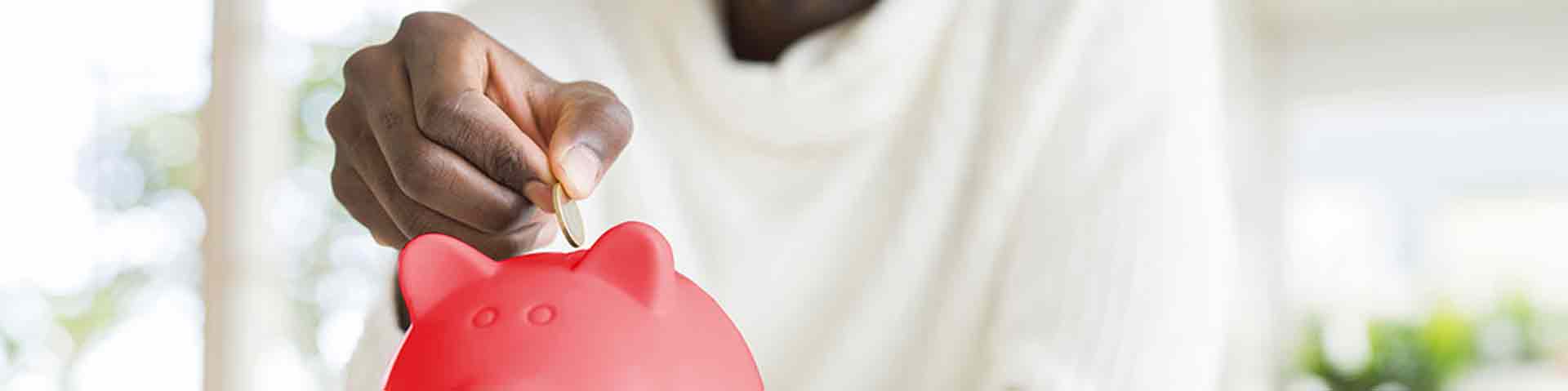 une homme insère une pièce dans une tirelire rouge