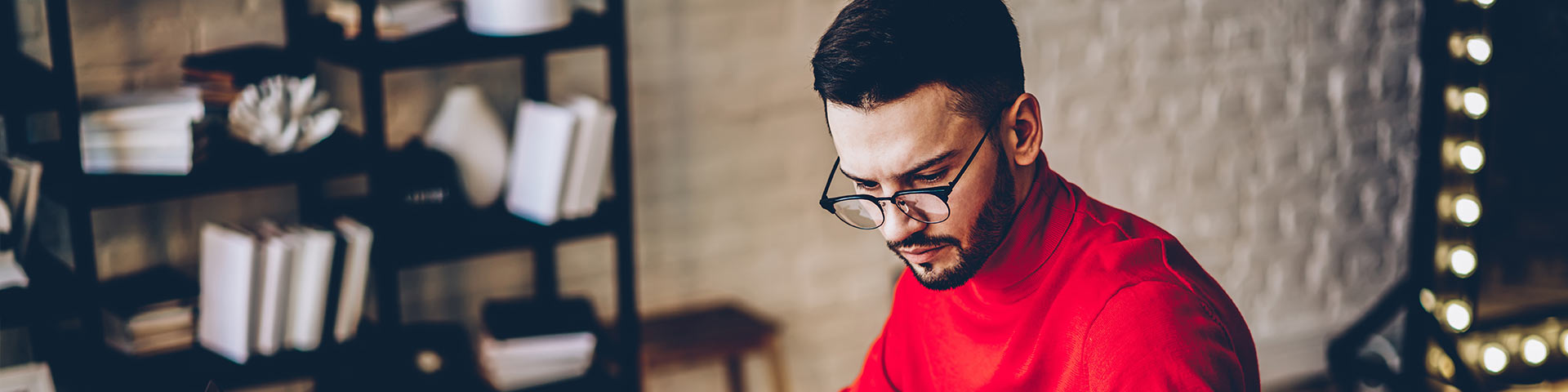 Homme trentenaire en pull rouge regardant des papiers sur son bureau