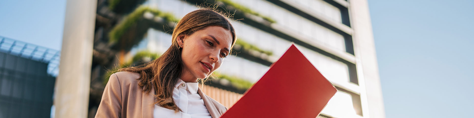 Femmes tenant une plaquette devant un immeuble d'habitation (article sur le dispositif Jeanbrun pour l'investissement locatif)