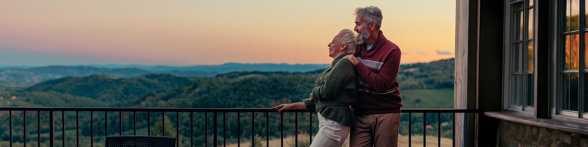 Un couple âgé regarde un coucher de soleil sur son balcon