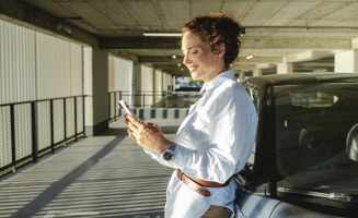 Une femme devant sa voiture qui regarde son téléphone