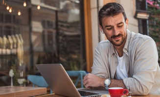 Un homme assis à la terrasse d'un bar avec son ordinateur
