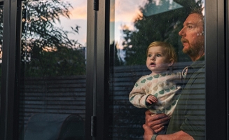 Père et sa jeune fille regardant le coucher du soleil au travers d'une baie vitrée