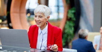 Une dame âgée en costume rouge qui consulte son ordinateur dans un open space