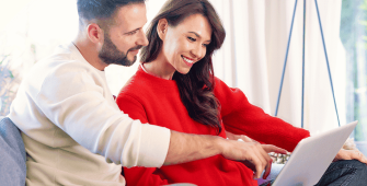 un couple assis sur un canapé, concentré sur l’écran d’un ordinateur portable