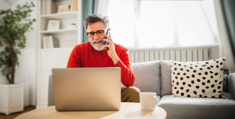 Un homme au téléphone consultant son ordinateur assis sur son canapé
