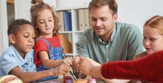 Un homme qui peint avec un groupe d'enfants autour d'une table