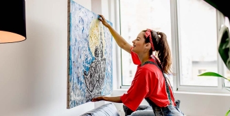 Une femme qui installe un tableau derrière son canapé 