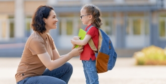 femme agenouillée devant une petite fille avec un cartable sur le dos