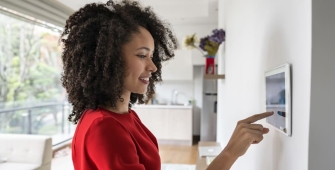 Une jeune femme 30-35 ans règle son thermostat connecté