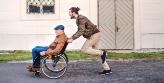 Un aidant familial pousse un homme âgé sur son fauteuil roulant