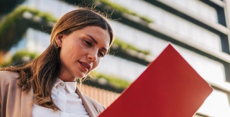 Femmes tenant une plaquette devant un immeuble d'habitation (article sur le dispositif Jeanbrun pour l'investissement locatif)