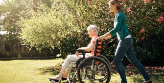 Une aidante familiale pousse une personne âgée en fauteuil roulant