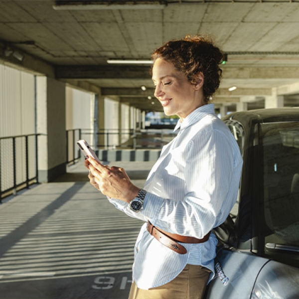 Une femme devant sa voiture qui regarde son téléphone