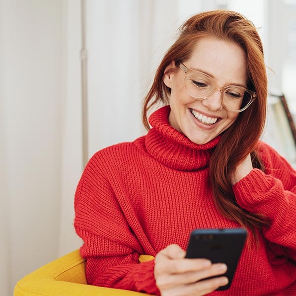 Jeune femme en pull rouge regardant son téléphone mobile