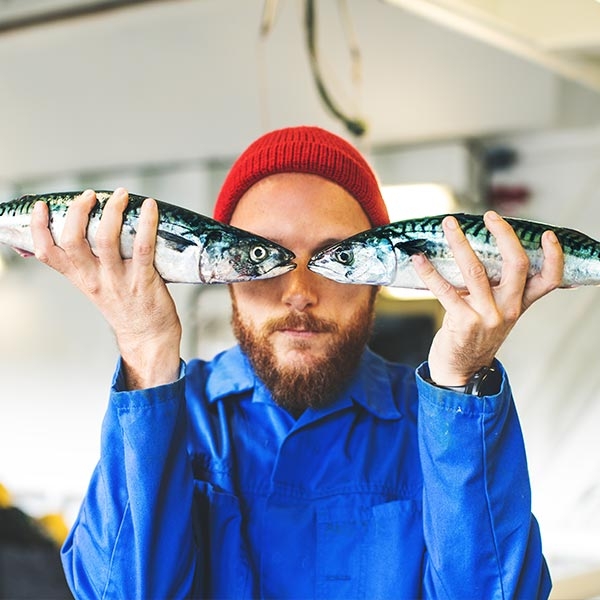 Jeune pêcheur tenant des poissons devant ses yeux, comme si les yeux des poissons étaient les siens
