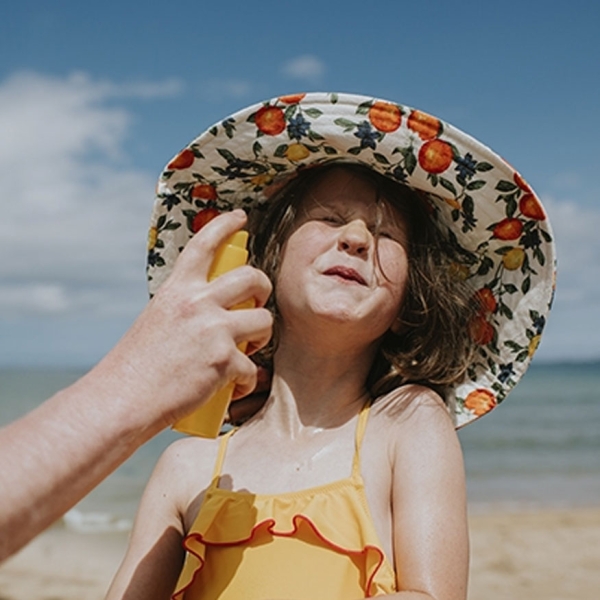 Jeune fille à la plage, son père lui met de la crème solaire