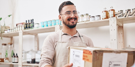 Un commerçant souriant remet un colis en point relais
