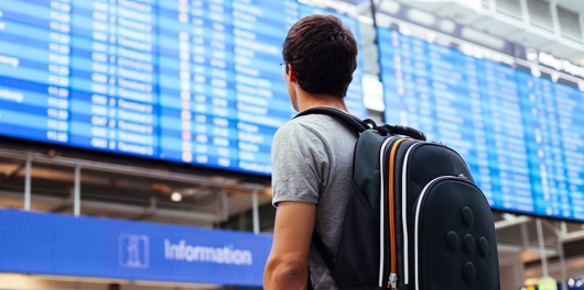 Jeune voyageur devant le panneau des départs d'un aéroport