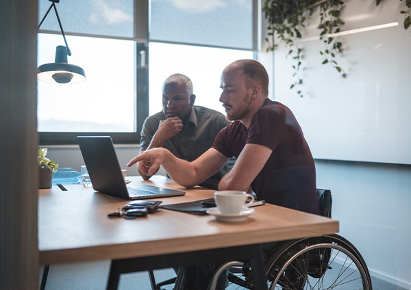 Deux homme au travail qui discutent, l'un est en fauteuil roulant