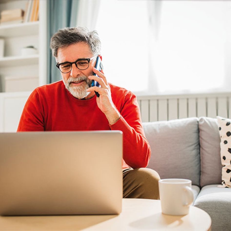 Un homme au téléphone consultant son ordinateur assis sur son canapé